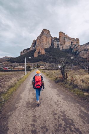 Hiker with backpack walking along rural road to cliff on gloomy day