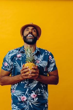 Happy male holding a pineapple to his chest in yellow studio