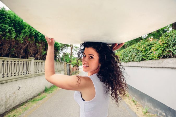 Smiling brunette woman holding surfboard over her head