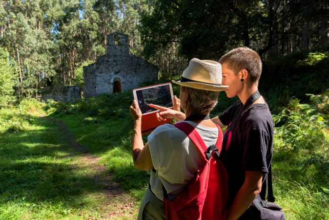 Younger woman hugging older woman taking picture on tablet in forest