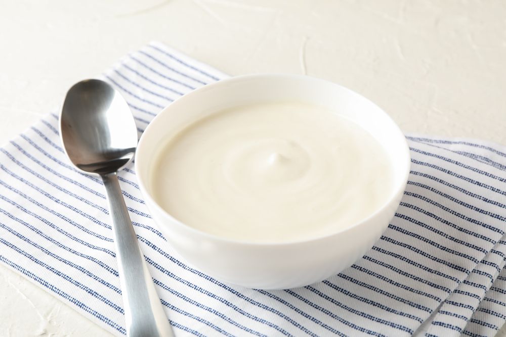 Bowl of sour cream yogurt, spoon and towel on cement background