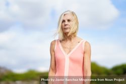 Portrait of stern older woman with  grey hair standing on wooden walkway near the coast 5qRga4
