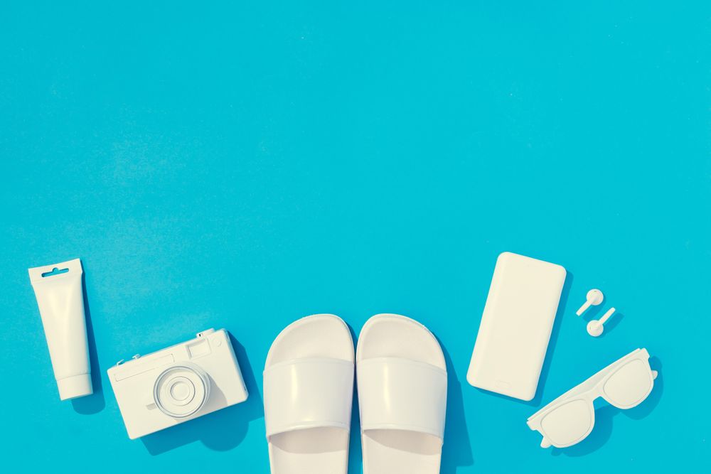 Summer objects of flip flops, sunglasses, camera, smart phone, EarPods on blue background