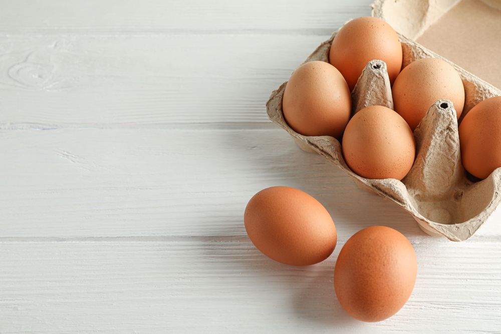 Brown chicken eggs in carton box on light background, space for text