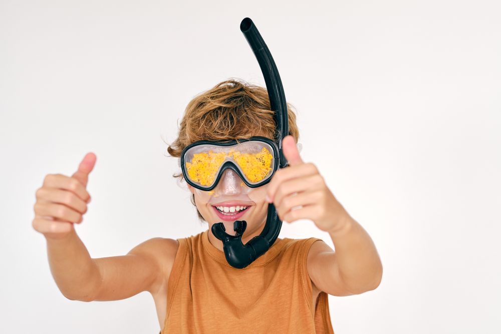 Smiling boy in snorkeling mask showing thumbs up