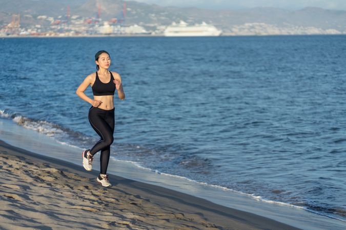 Sportswoman running on sandy sea beach on sunny day