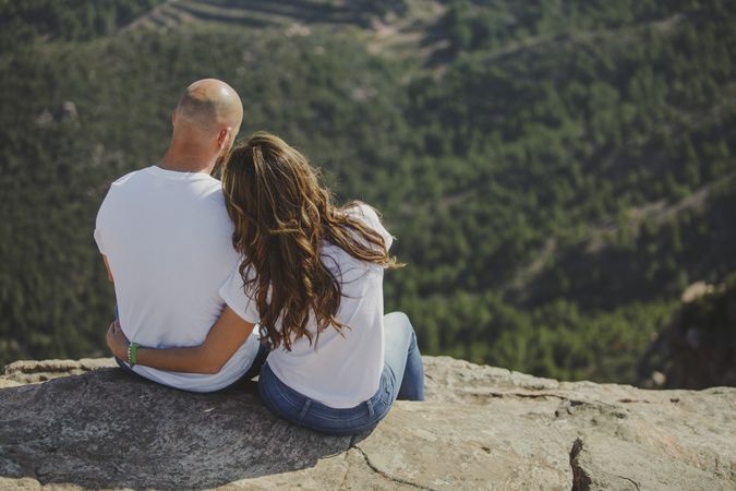 Happy couple sitting at mountain cliff