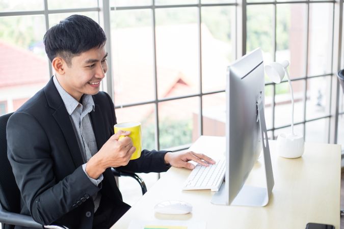 Male smiling looking at screen in the office with yellow mug
