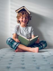 Cheerful preschool boy reading book on bed