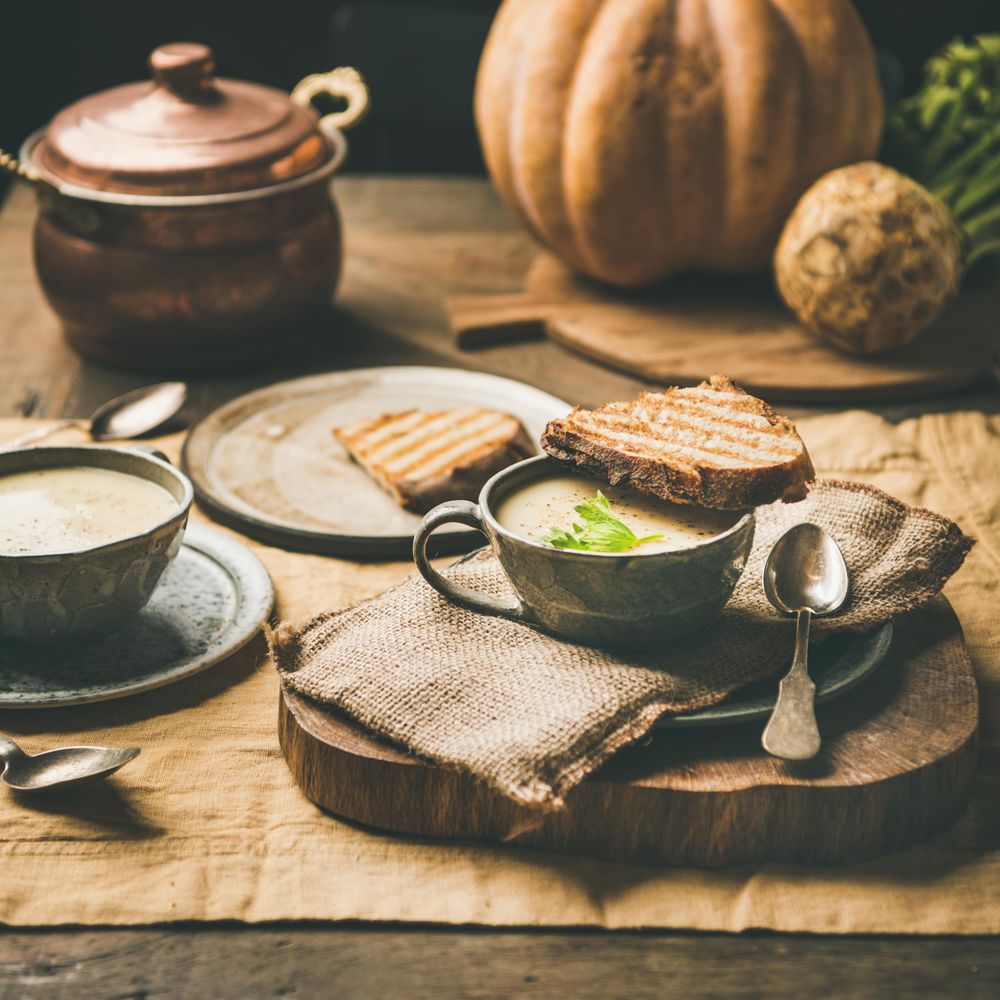 Celery soup in cups with toast, spoon, cloth napkin, on wooden board, square crop