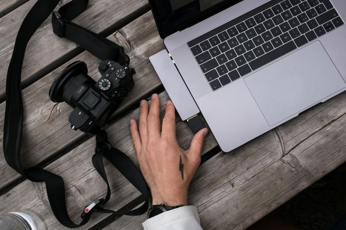 Tattooed hands with camera and laptop