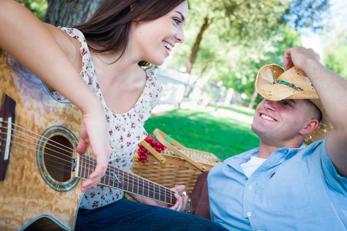 Young Adult Playing Guitar with Boyfriend In The Park.