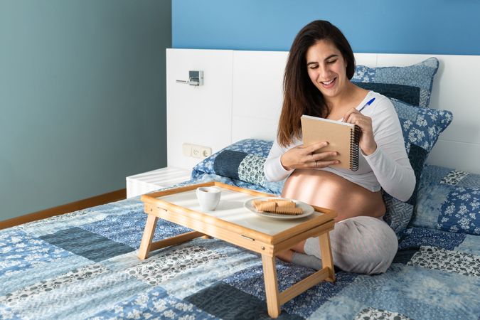 Pregnant woman having breakfast and taking notes in notepad