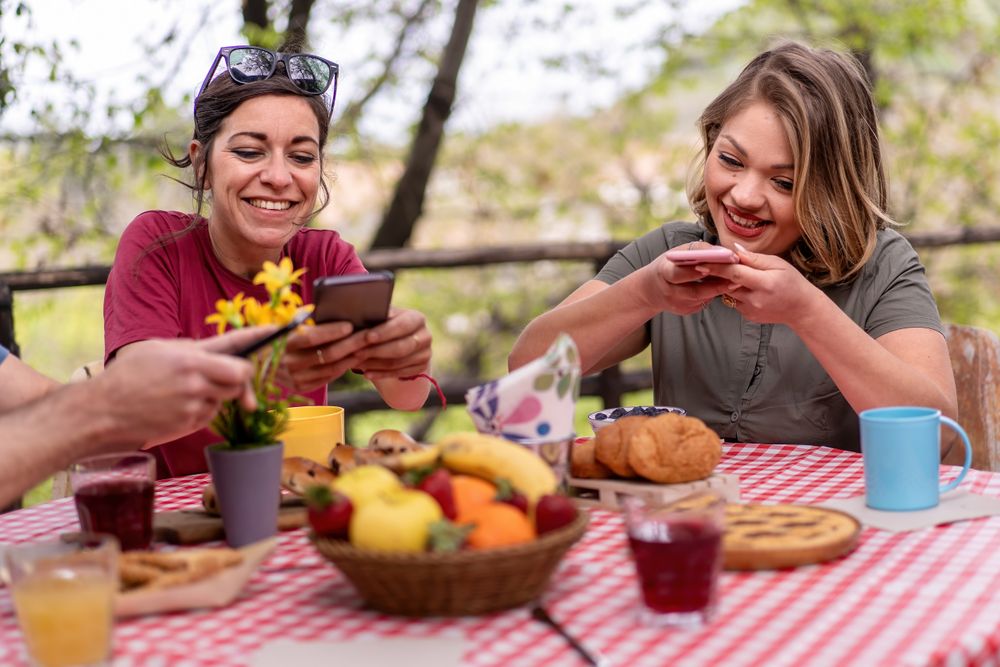 Two women taking picture of their brunch setup on smartphones
