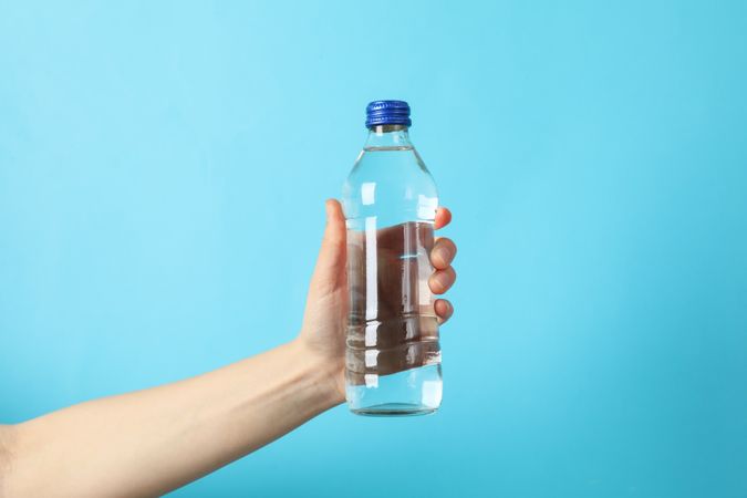 Hand holding plastic water bottle in blue space