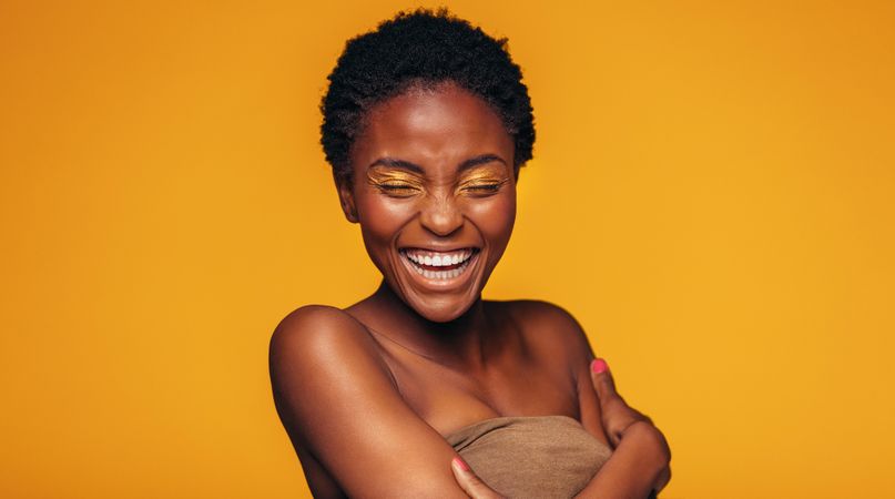 Young woman laughing against yellow background