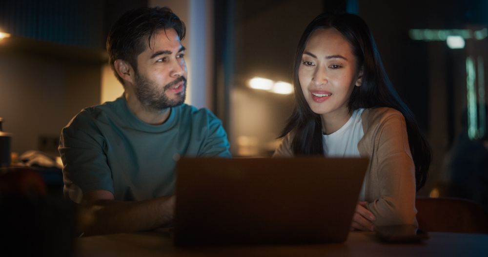 Portrait of Young Couple Using Laptop Computer While Sitting in the Kitchen at Home.