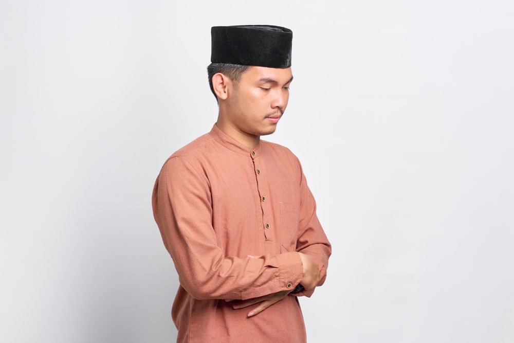 Solemn Muslim man looking down in kufi head wear with arms crossed