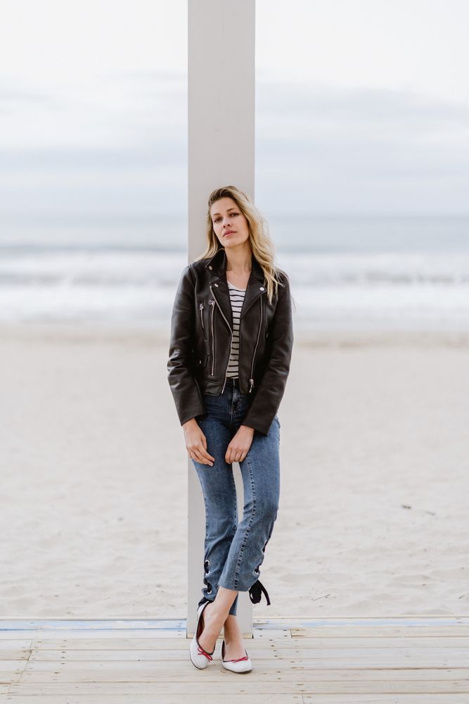 Smiling trendy woman leaning on white pillar on seashore