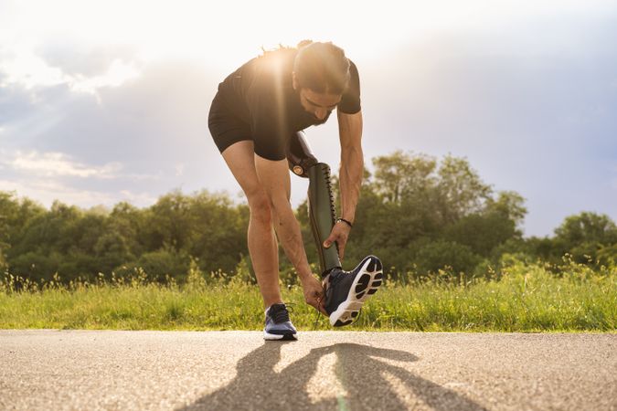 Man athlete with prosthetic leg tying his shoes outdoors - ready for tryout