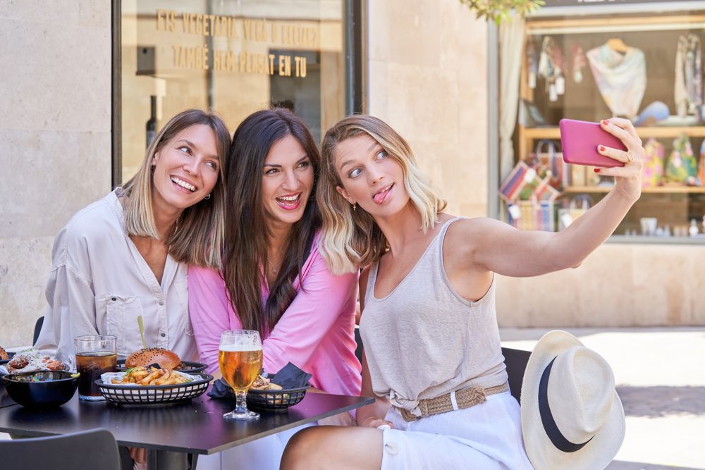 Women having fun in outdoor restaurant and taking selfie