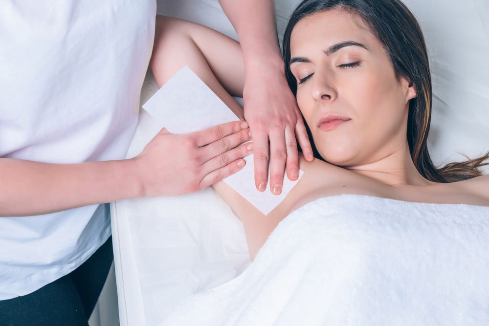 Beautician waxing woman's underarm in a beauty salon
