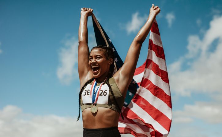 Female runner with a medal celebrating victory holding American flag over her head
