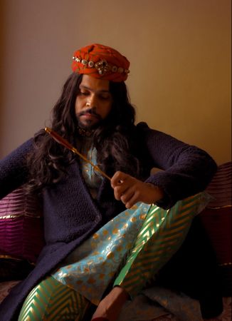 Indian man with long hair sitting on floor holding a stick