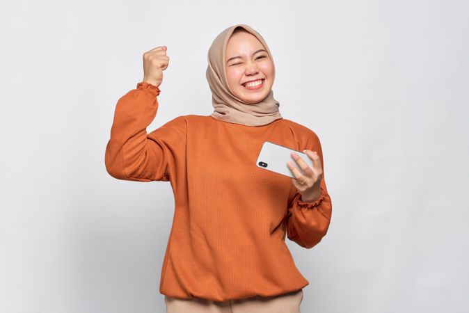 Elated Muslim woman holding her smartphone with fist up after winning
