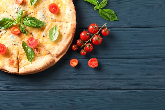 Cheese pizza with tomatoes and basil on wooden background, copy space