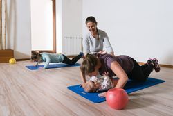 Fitness instructor helping mother with push ups