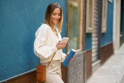 Smiling woman with reusable bottle using smartphone on street