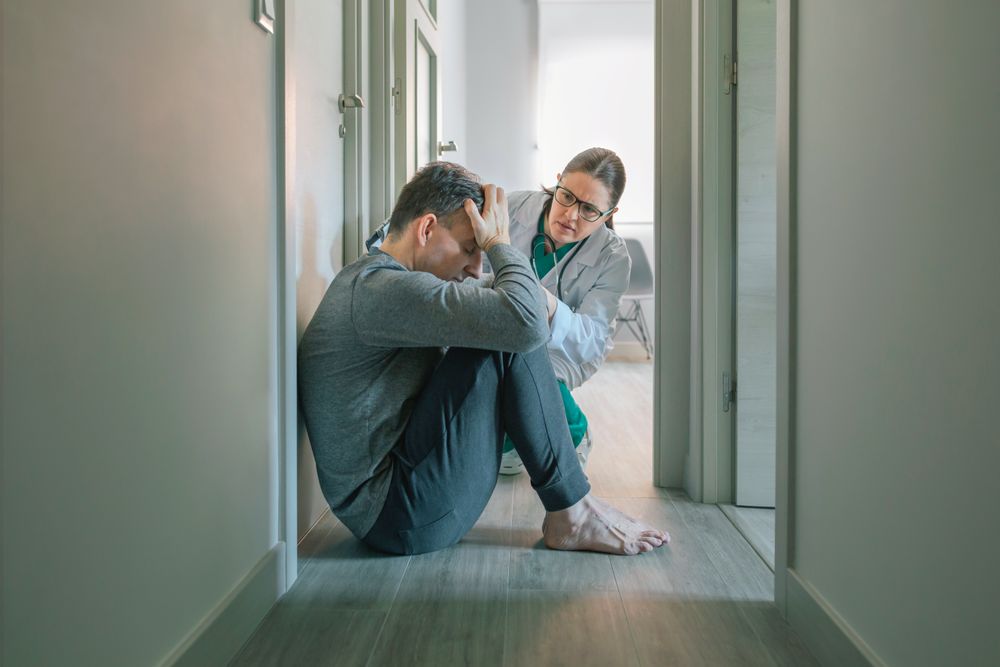 Psychiatrist reassuring and helping to patient sitting on room floor