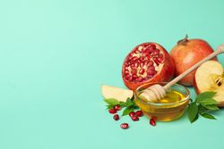 Open pomegranate, apple half, and honey in mint room with copy space