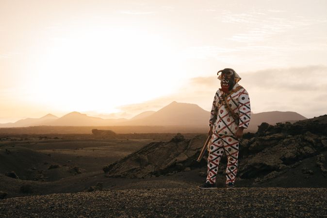 Person in brightly patterned clothes and devil mask standing on volcanic hills in Lanzarote at dusk