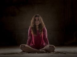 Young woman in lotus pose between sand in darkness