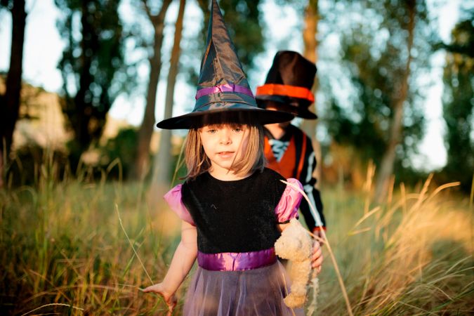 Little girl in witch costume leading her brother in the long grass