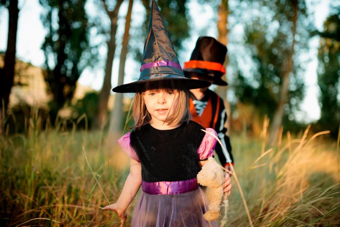 Little girl in witch costume leading her brother in the long grass