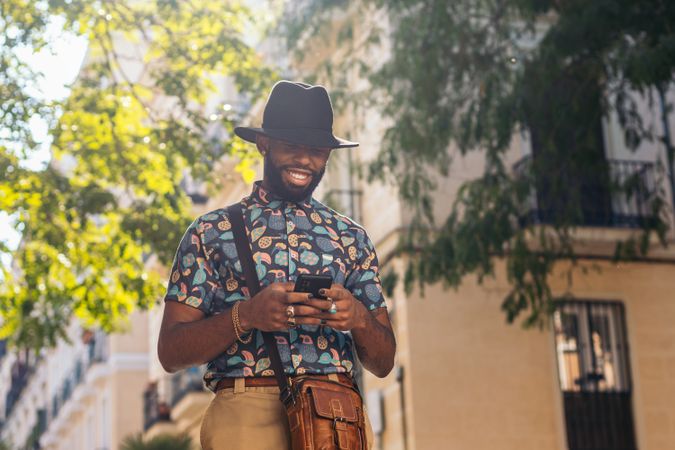 Stylish Black man walking on the city street using smartphone