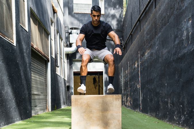 Concentrated athlete jumping on wooden box