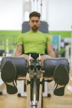 Active male in green t-shirt working out quads using gym equipment