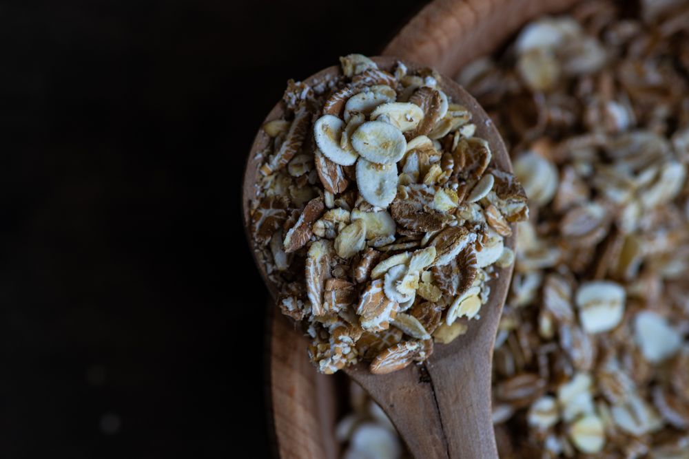 Close up of wooden spoon with oat grains over bowl