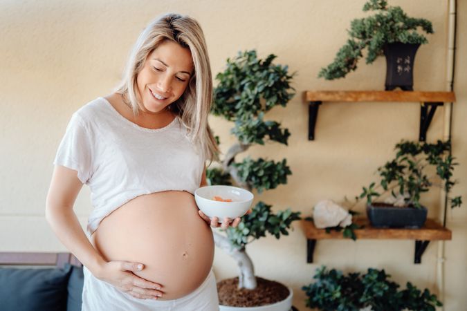 Smiling pregnant woman holding belly at home