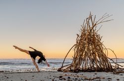 Young woman dancing on shore near water and wooden twigs placed for campfire