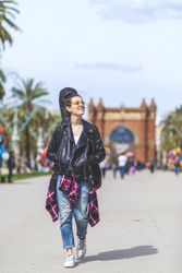 Front view of a young laughing hipster woman walking in a park in sunny day while looking away
