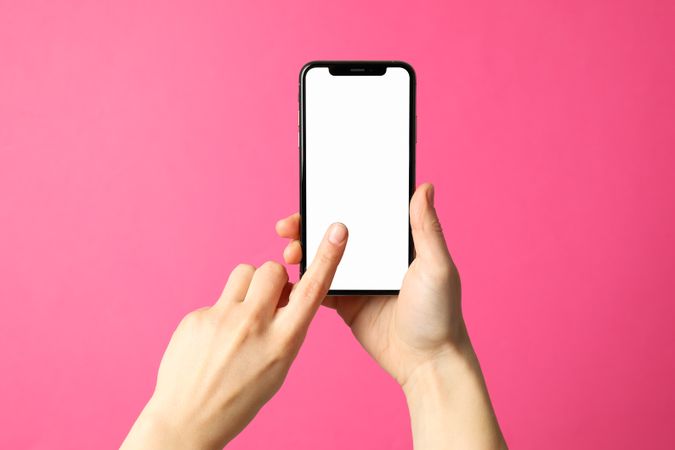 Female hands hold phone on pink background. Empty screen