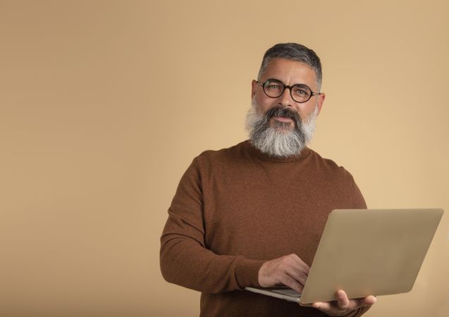 Portrait of smiling middle aged man holding a laptop standing against yellow background