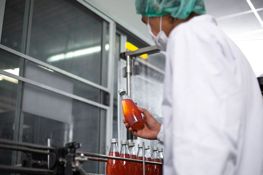 A factory worker is holding a bottle of fruit juice to inspect its quality inside a beverage manufacturing facility.