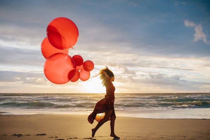 Young woman running along the beach holding a bunch of balloons