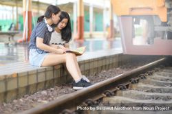 Two female travelers look at maps on a train platform 4BePk5